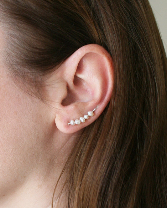 Close-up of an ear wearing a pearl earring with a neutral background