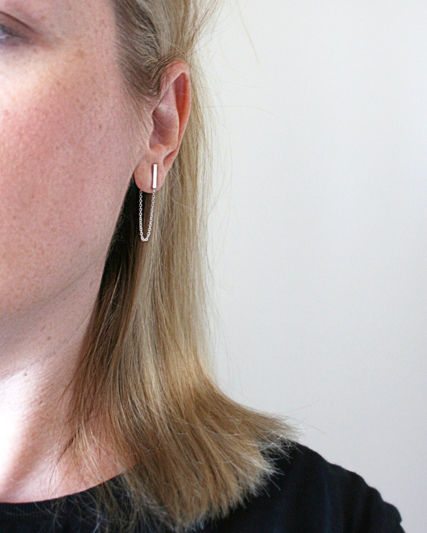 Close-up of a person wearing a silver hoop earring against a plain background