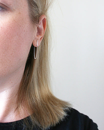 Close-up of a person wearing a silver hoop earring against a plain background