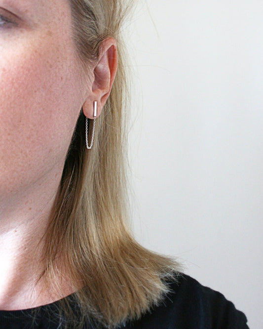 Close-up of a person wearing a silver hoop earring against a plain background