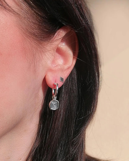 Close-up of an ear wearing a silver earring with a geometric design.