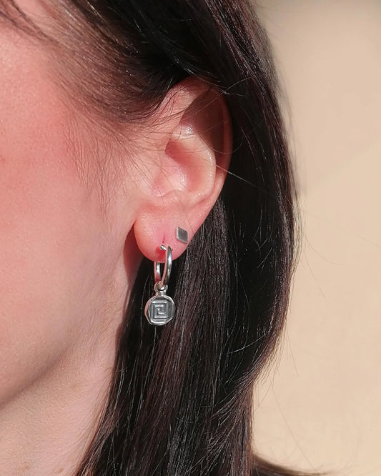 Close-up of an ear wearing a silver earring with a geometric design.