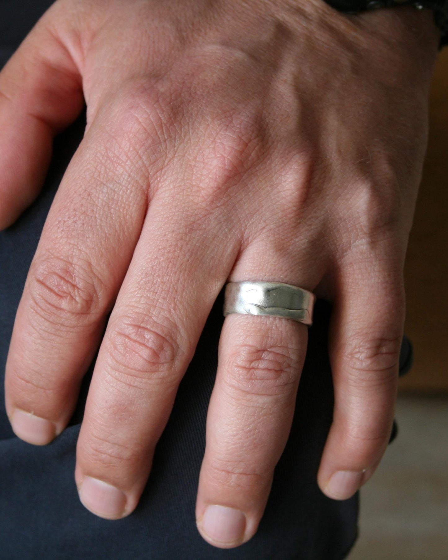 Hand wearing a silver ring with a blurred background