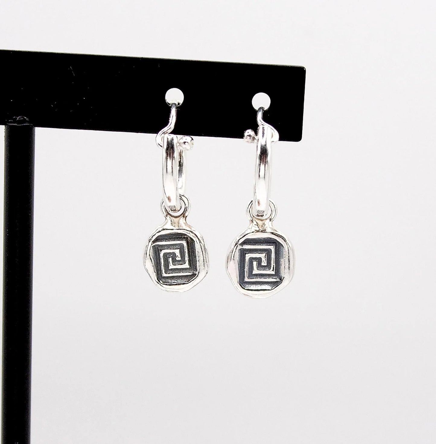 Silver hoop earrings with geometric spiral pendants on display stand