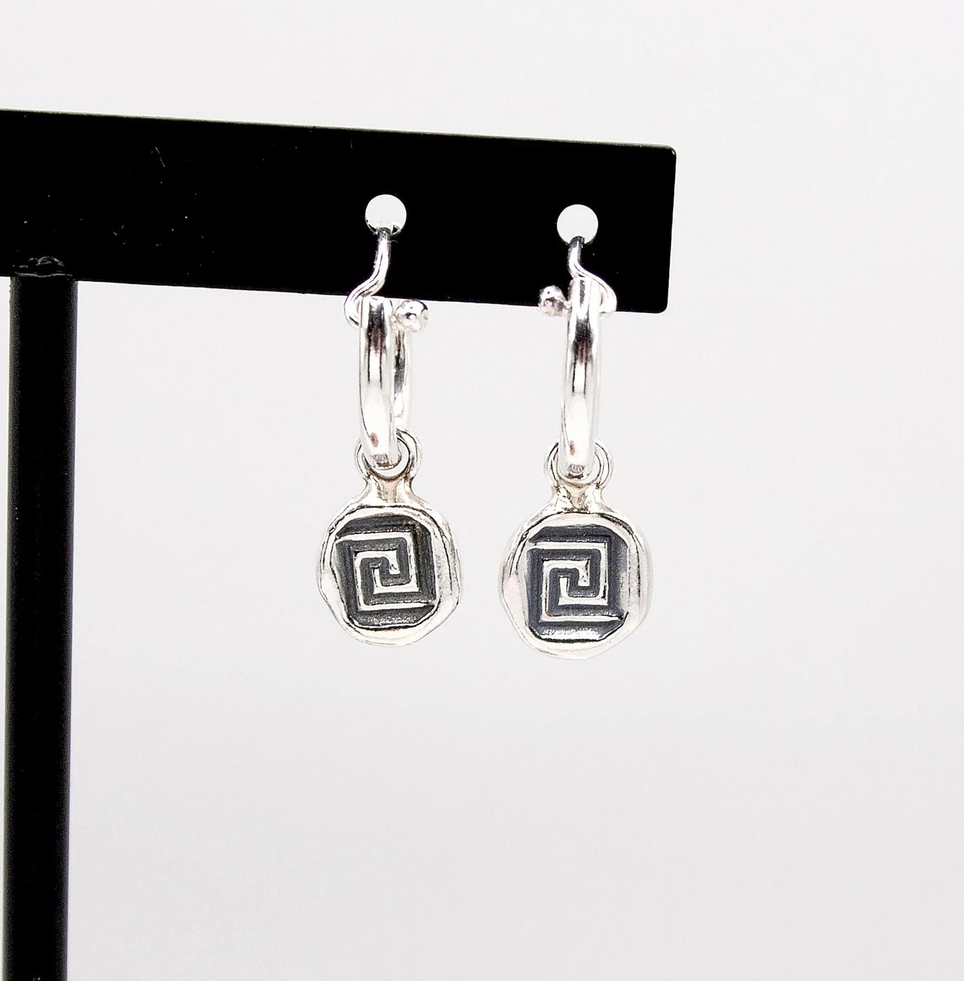 Silver hoop earrings with geometric spiral pendants on display stand