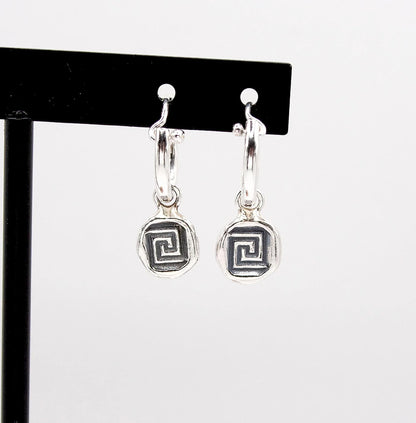 Silver hoop earrings with geometric spiral pendants on display stand