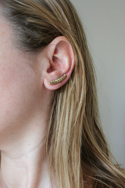 Close-up of an ear wearing a gold earring with a plain background