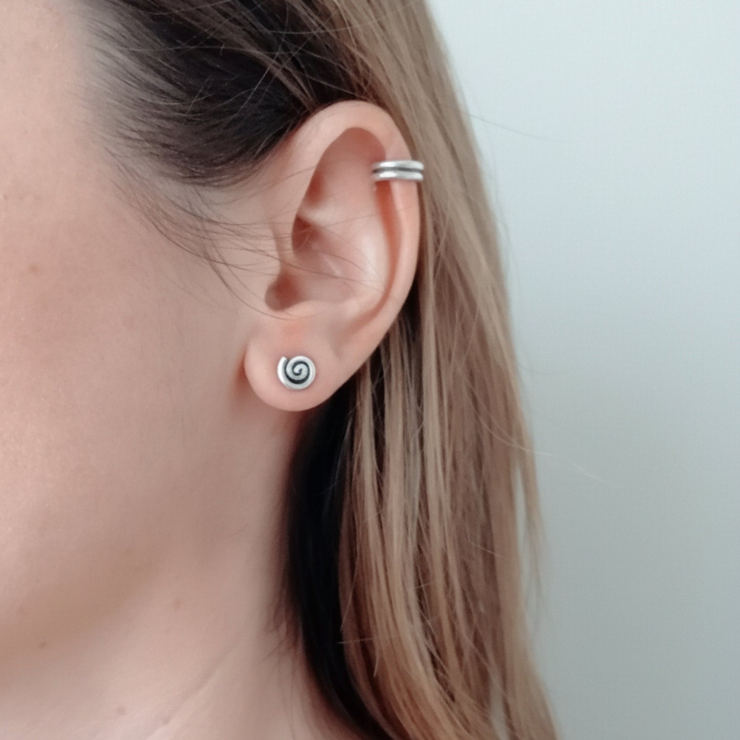 Close-up of an ear with a silver spiral earring on a plain background