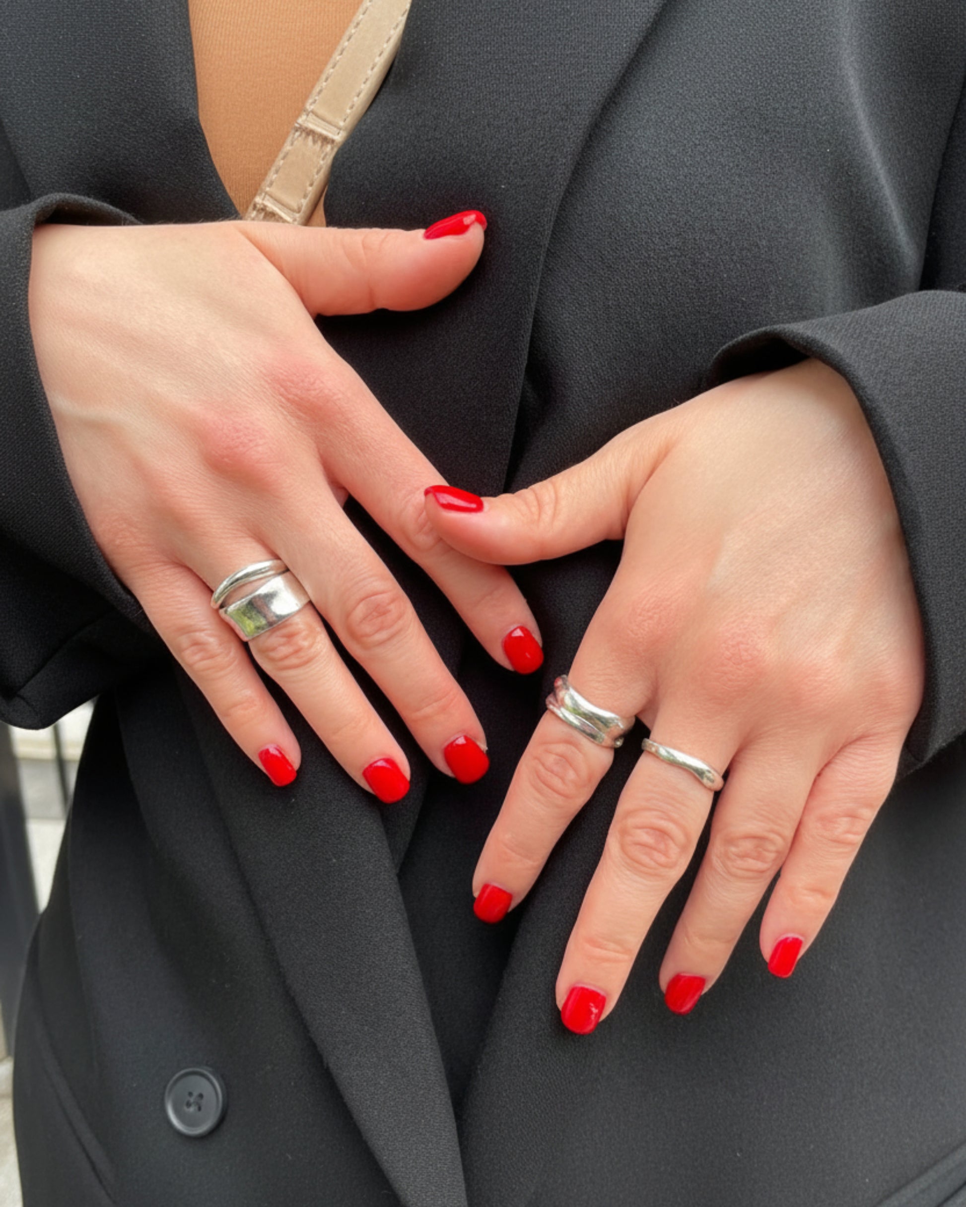 Close-up of two hands with red nail polish and silver rings on a dark background