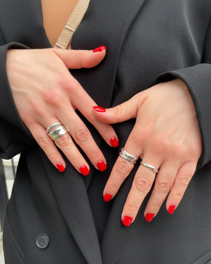 Close-up of two hands with red nail polish and silver rings on a dark background