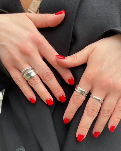 Close-up of two hands with red nail polish and silver rings on a dark background