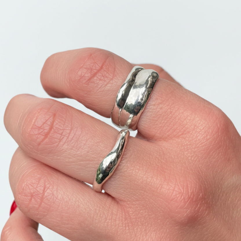 Silver ring with wavy design on a finger against a white background