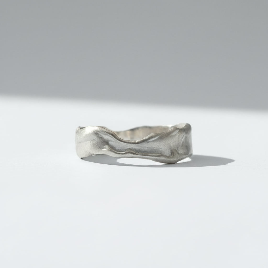 A textured, wavy band ring in a silver-toned metal, photographed against a seamless white background.