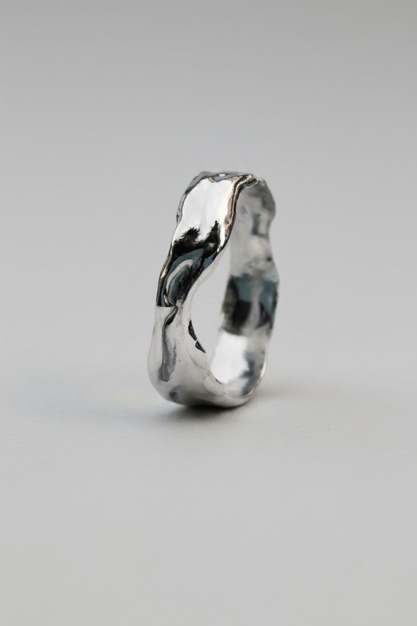 A polished silver ring with an organic, wavy, fluid contour, shown on a clean white background.