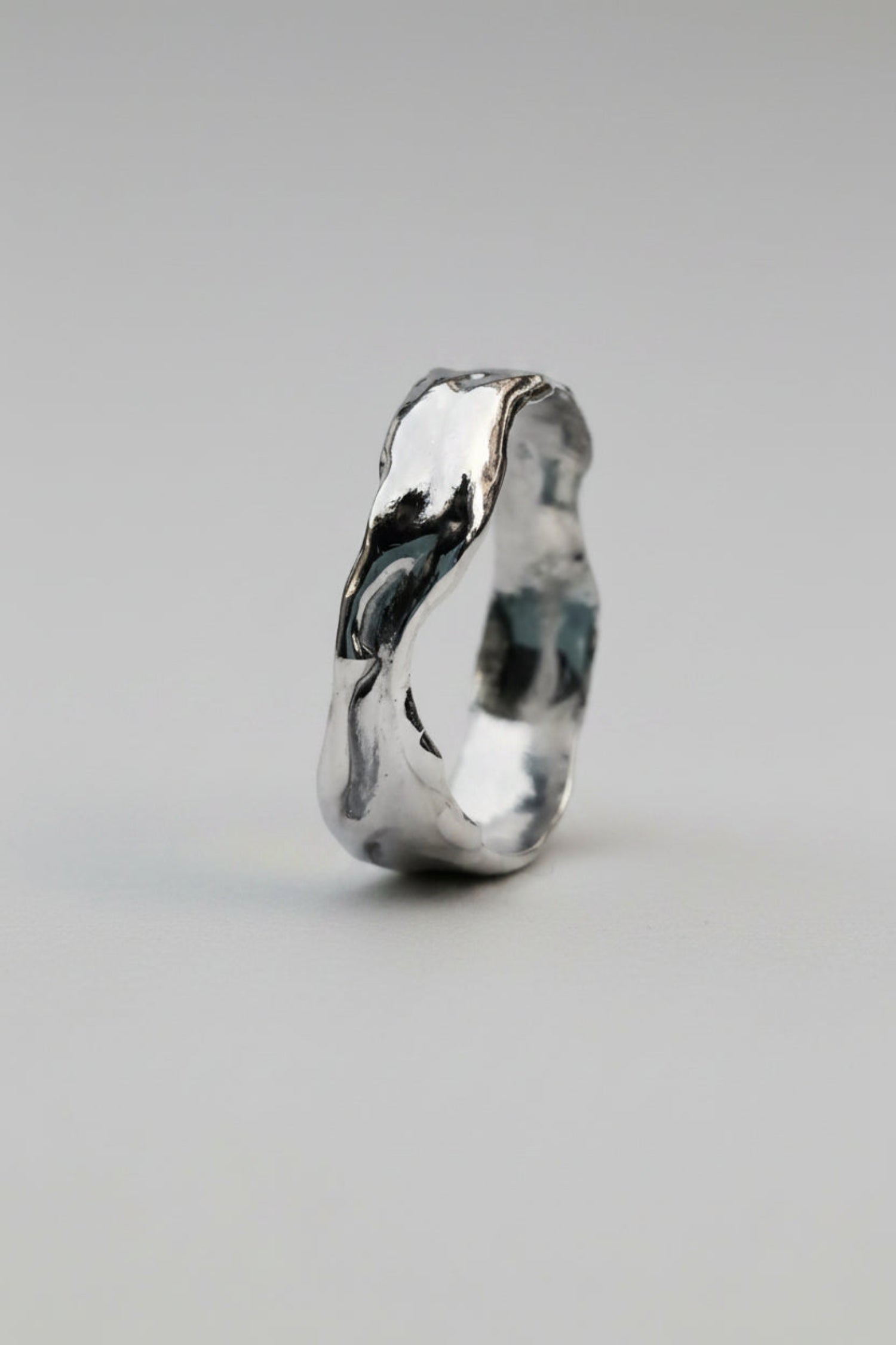 A polished silver ring with an organic, wavy, fluid contour, shown on a clean white background.