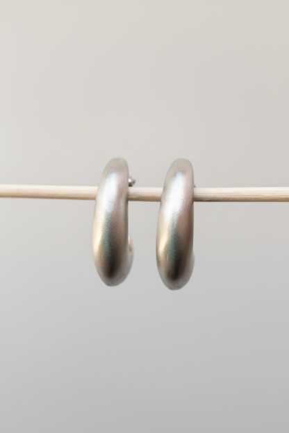 A pair of thick, polished silver hoop earrings hanging from a thin horizontal wire against a plain light gray background.