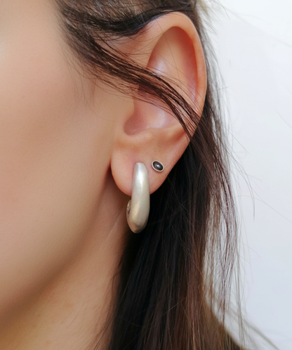 A close-up of a person's ear wearing a large, curved, cream-colored hoop earring and a small black oval stud earring.