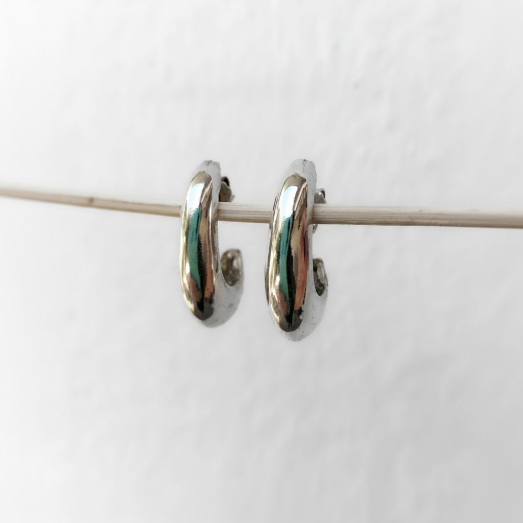 A pair of polished silver huggie hoop earrings hanging from a thin horizontal wire against a plain white background.