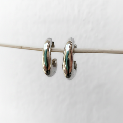 A pair of polished silver huggie hoop earrings hanging from a thin horizontal wire against a plain white background.