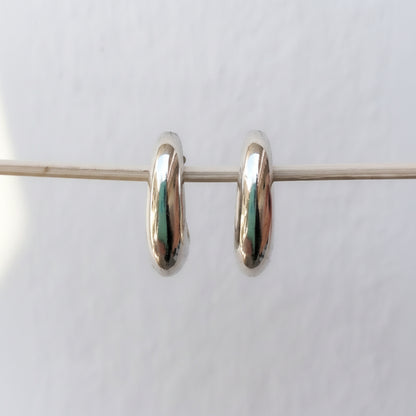 A pair of small, polished silver hoop earrings suspended horizontally on a thin wire against a plain white background.