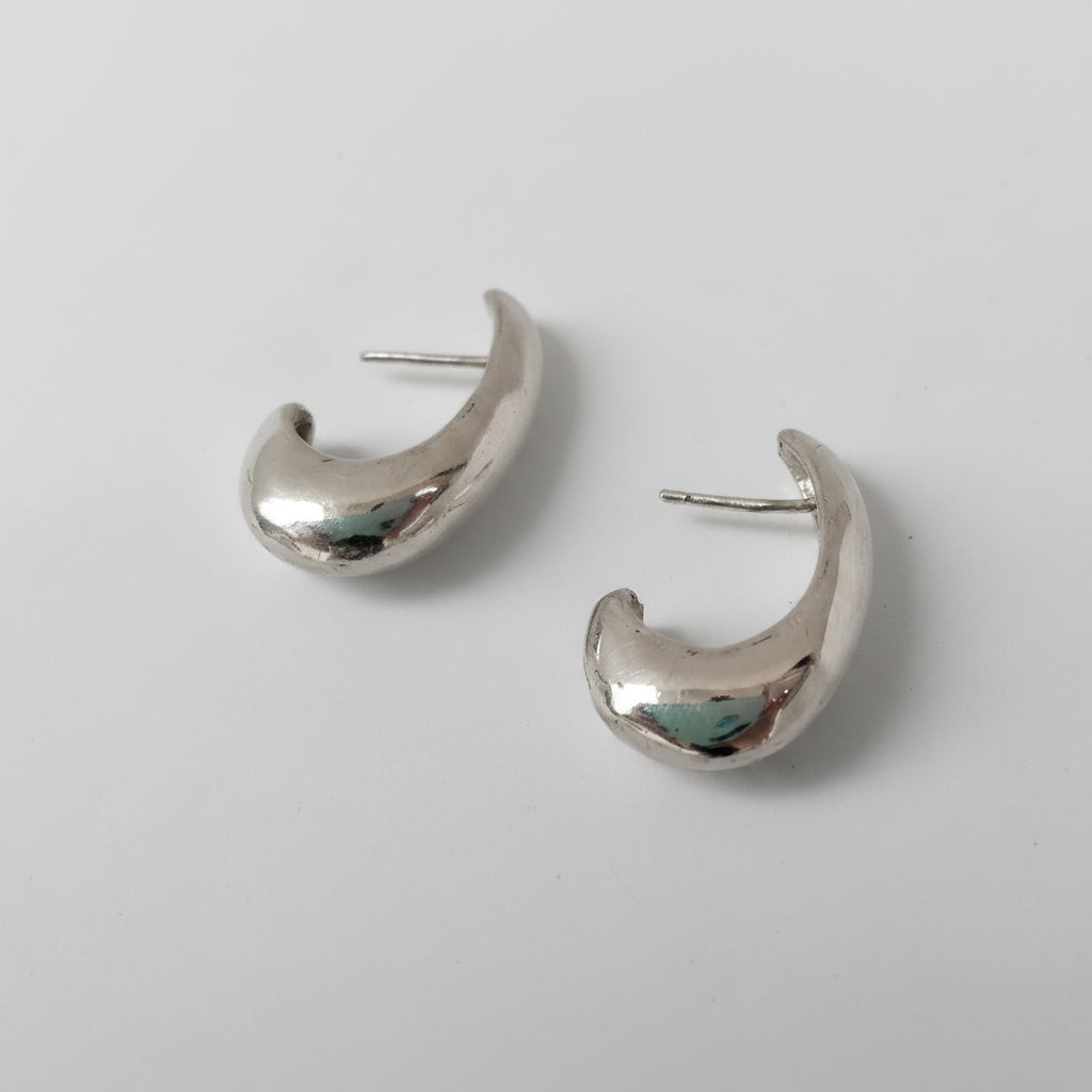 A pair of polished silver crescent-shaped hoop earrings with flat posts, displayed on a clean white background.