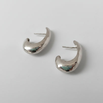 A pair of polished silver crescent-shaped hoop earrings with flat posts, displayed on a clean white background.