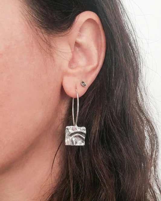 Close-up of a person wearing a silver earring with a textured square design.