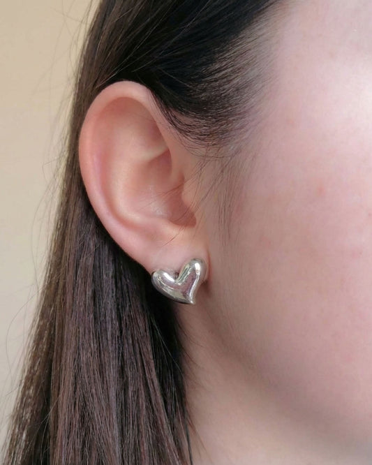 Silver heart-shaped earring worn by a person with dark hair.
