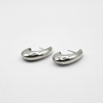A pair of silver-toned, organic-shaped hoop earrings on a plain white background.