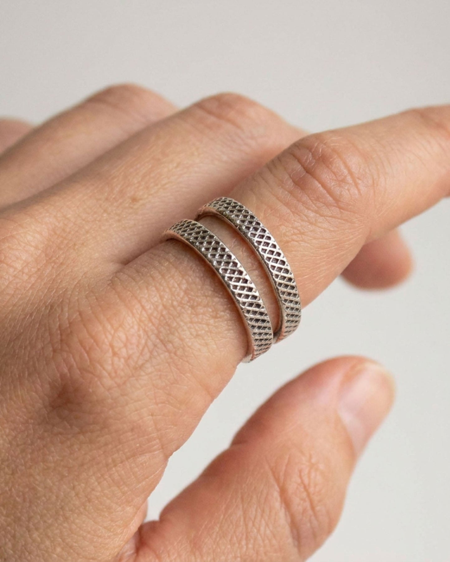 Hand wearing two silver textured rings on a light background