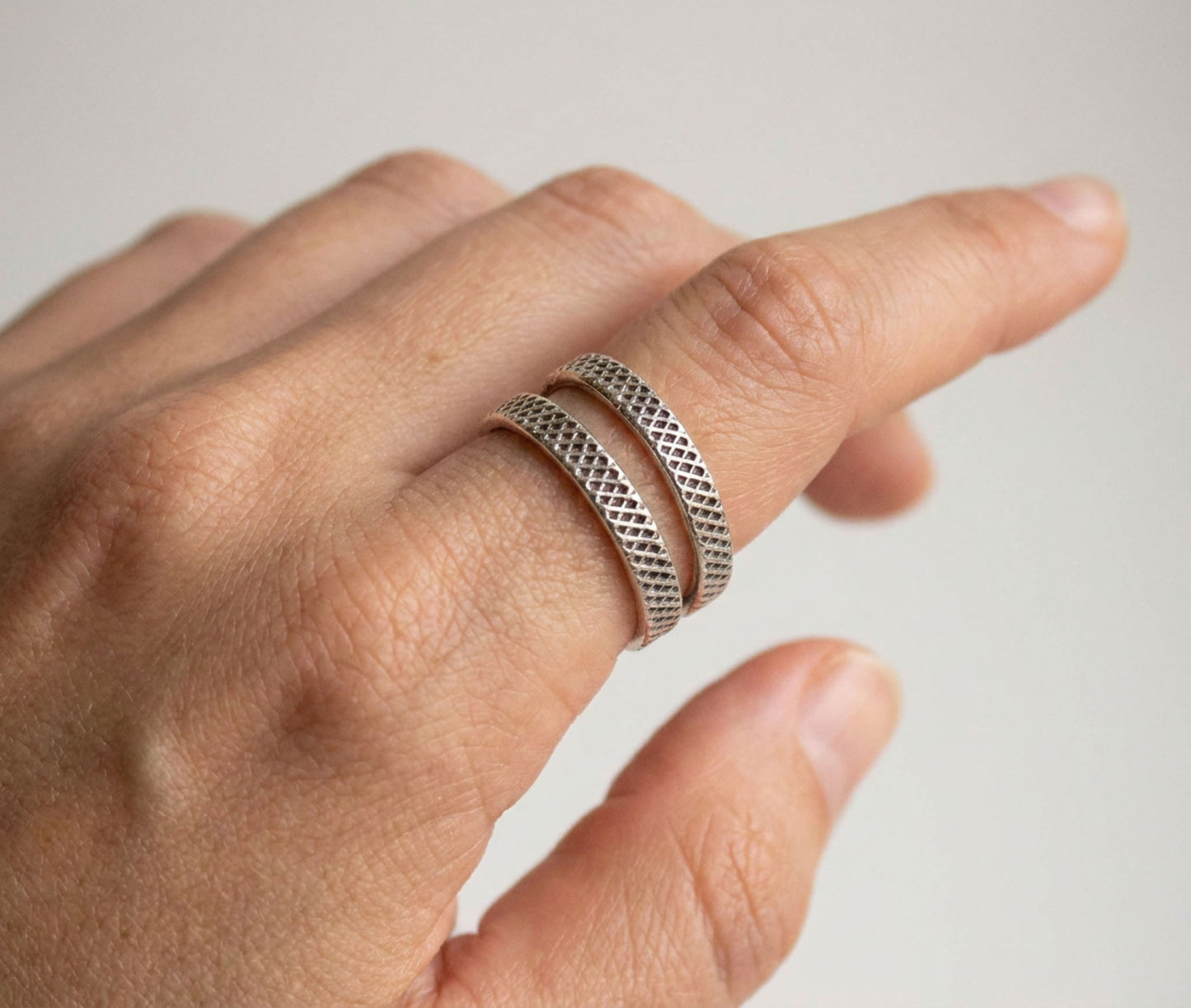 Hand wearing two silver textured rings on a light background