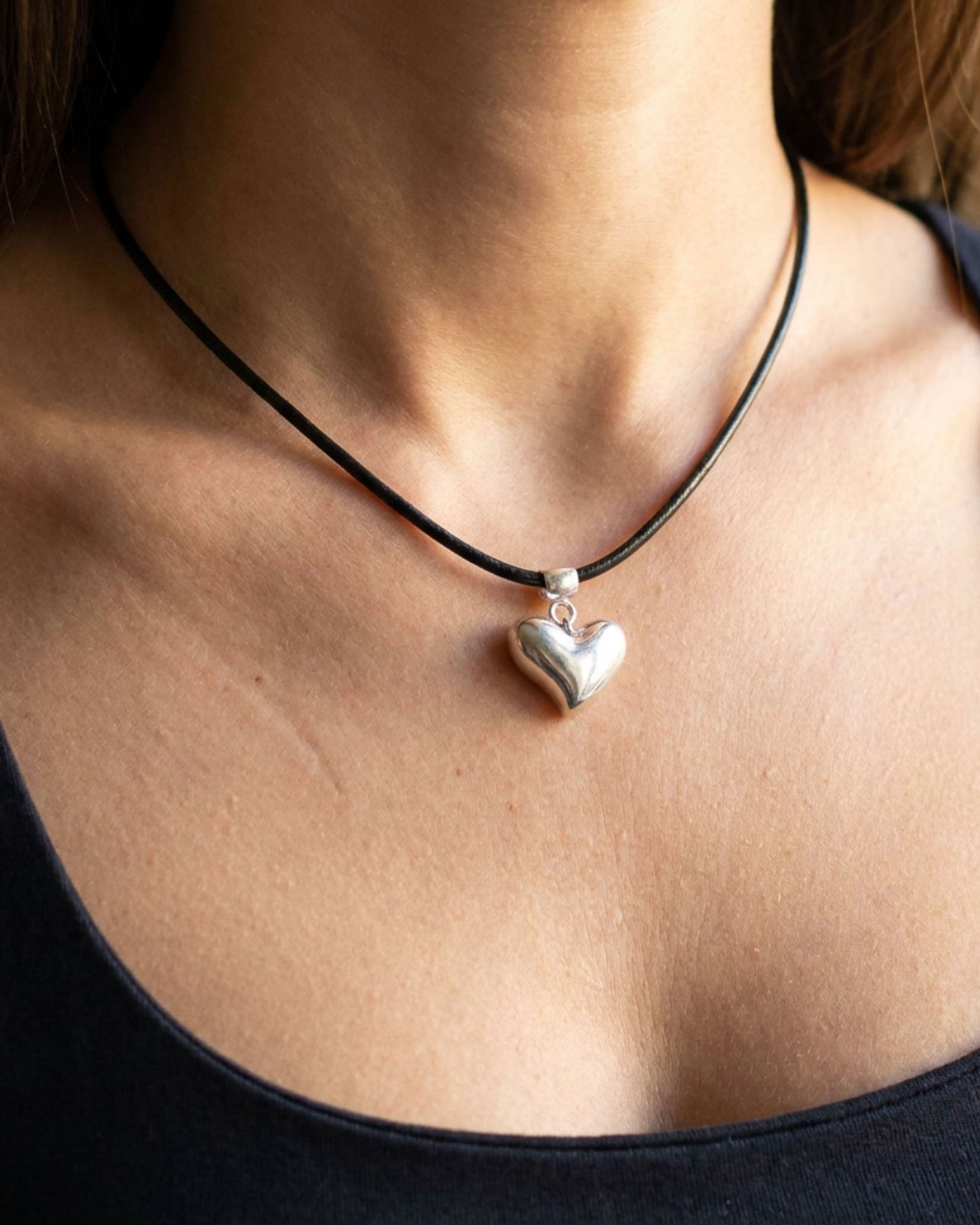 Heart-shaped pendant on a black cord necklace worn by a person.