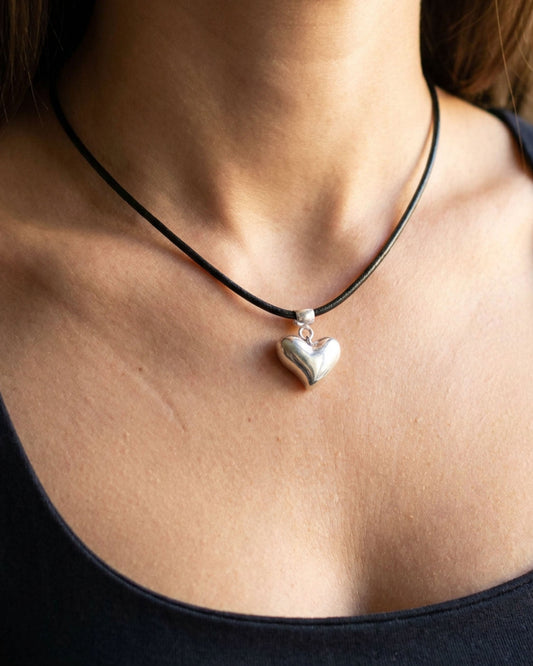 Heart-shaped pendant on a black cord necklace worn by a person.