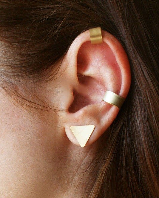 Gold triangle earring worn on an ear with a blurred background