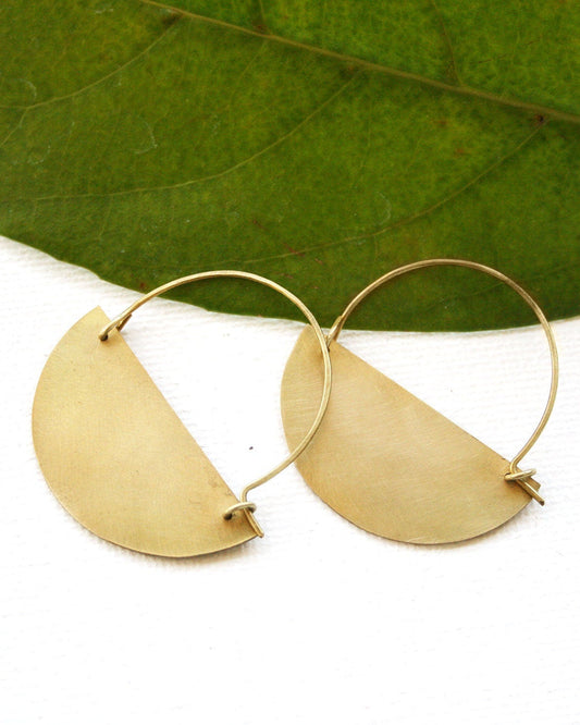 Gold earrings on a white background with a green leaf