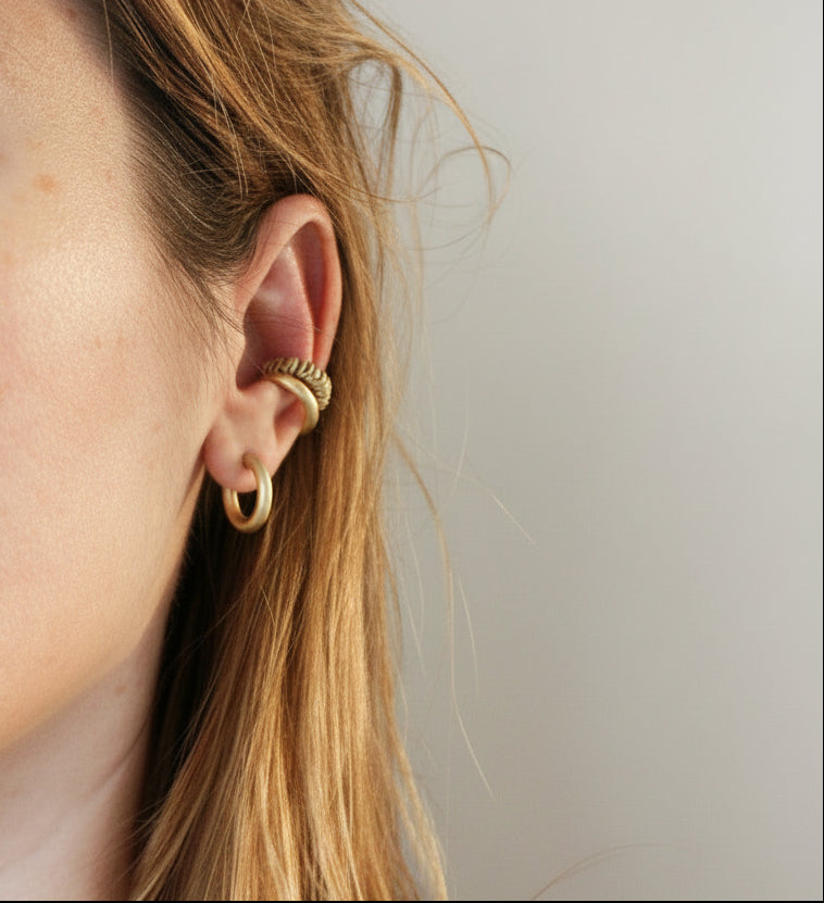 Close-up of an ear wearing a gold earring against a plain background