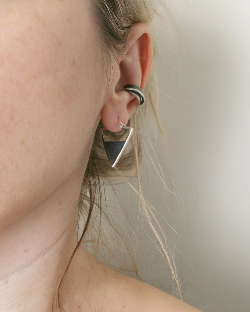 Close-up of an ear wearing a silver earring with a neutral background