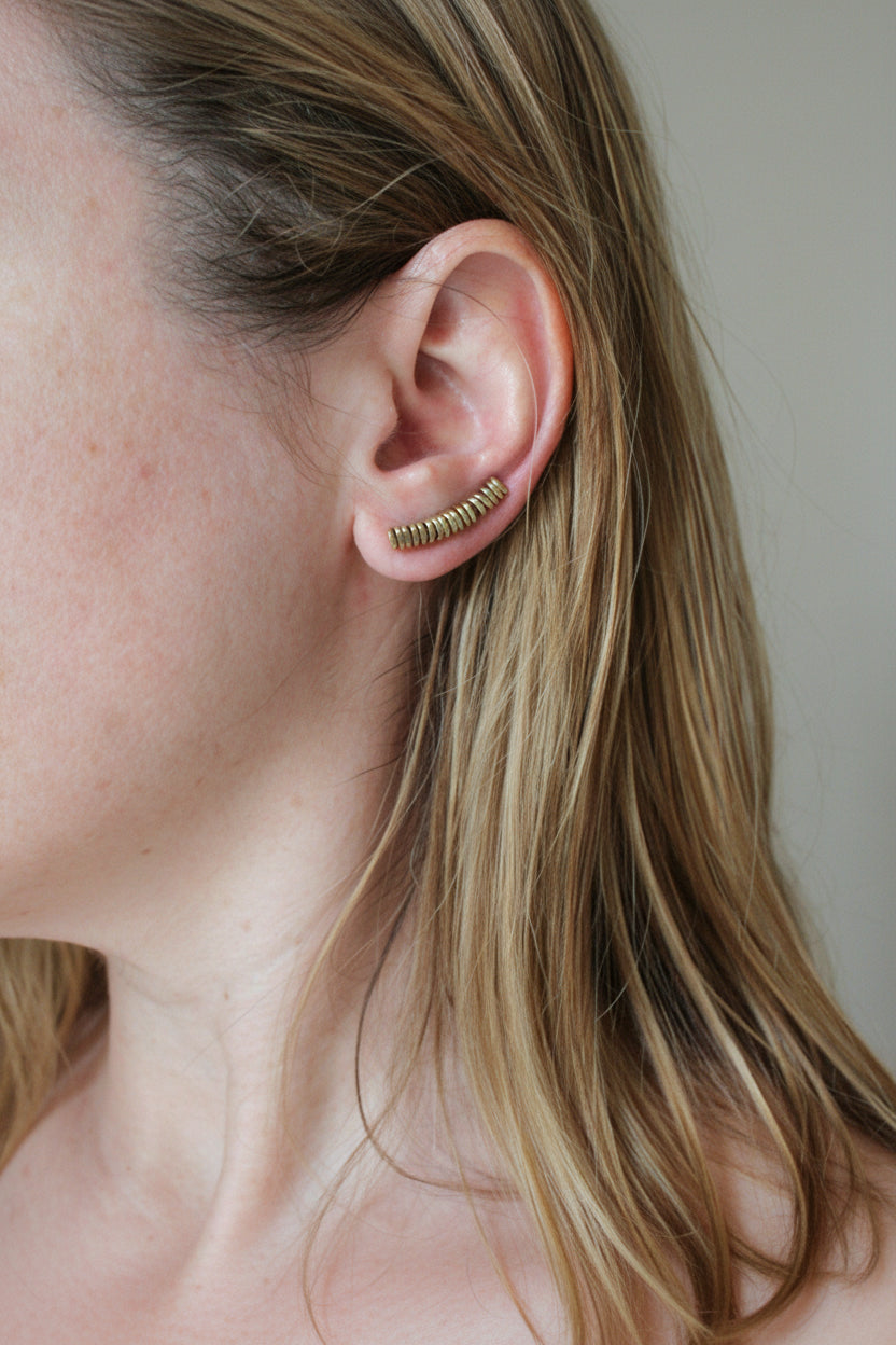Close-up of a person wearing gold hoop earrings with a neutral background