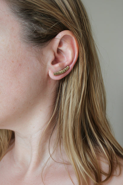 Close-up of a person wearing gold hoop earrings with a neutral background