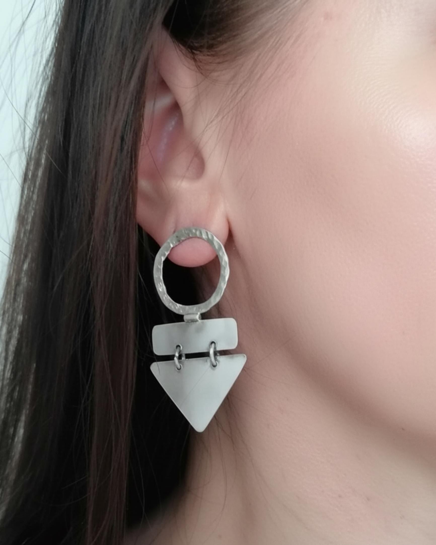 Close-up of a person wearing a unique silver earring with geometric design.