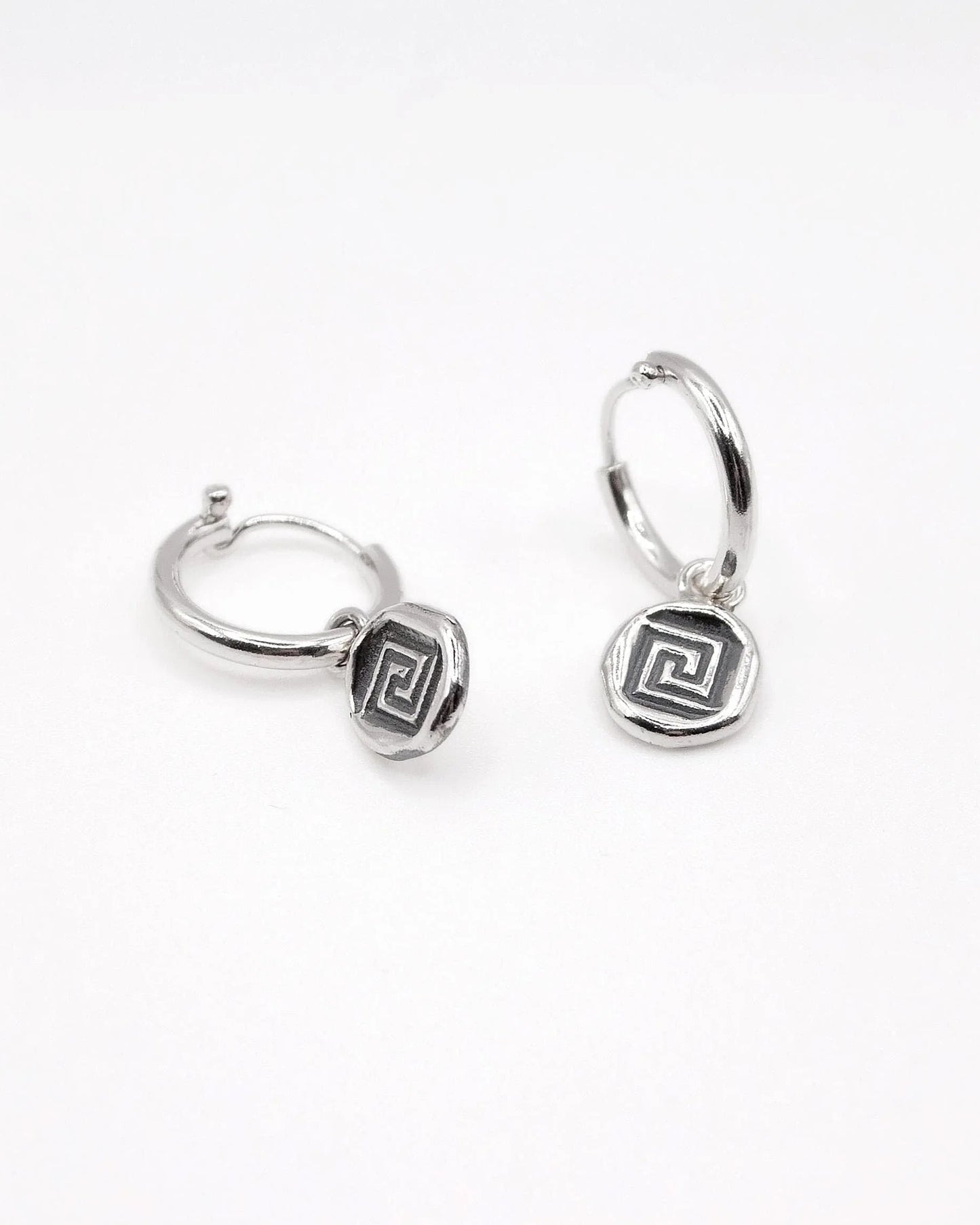 Silver hoop earrings with geometric Greek key charm on white background