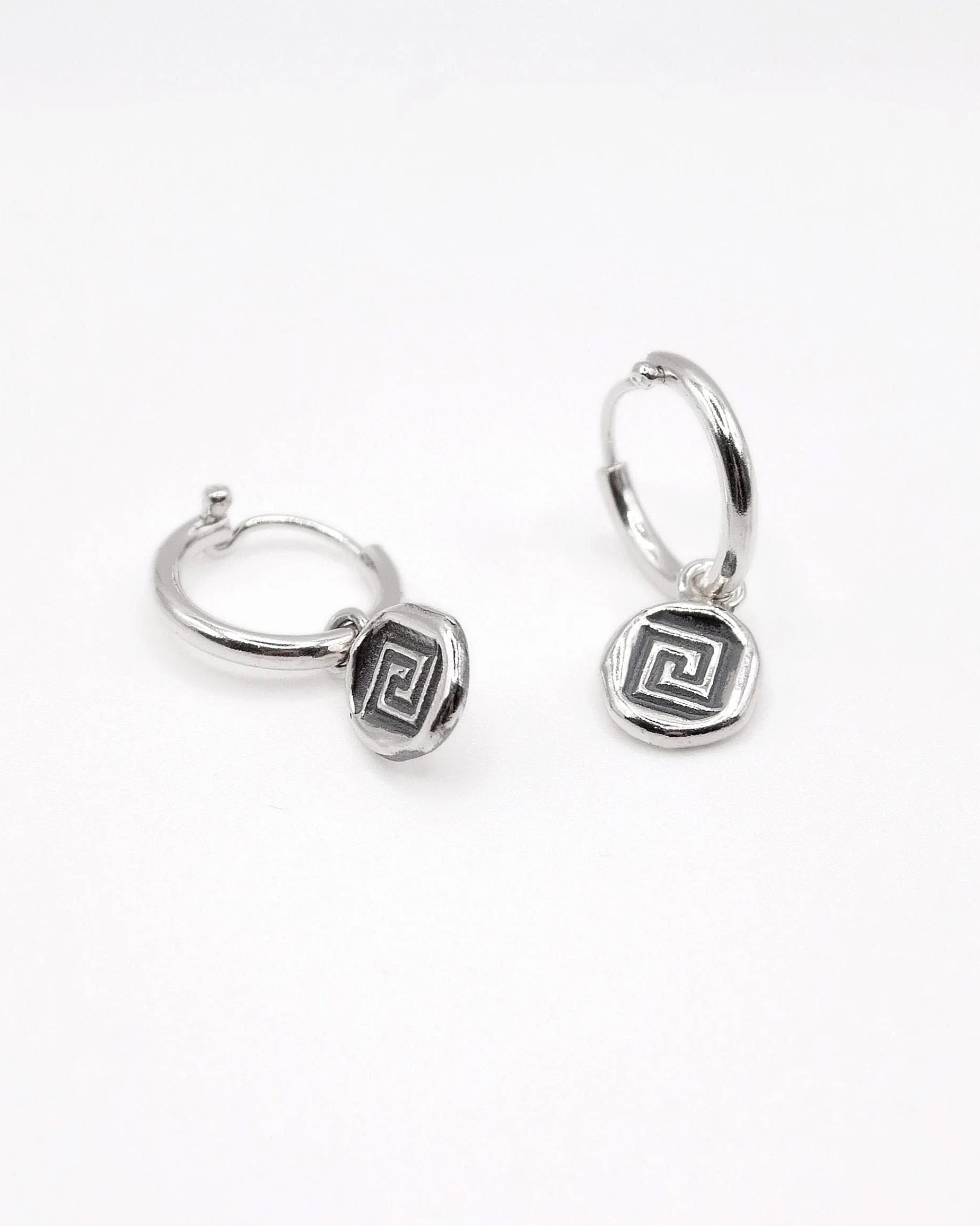 Silver hoop earrings with geometric Greek key charm on white background
