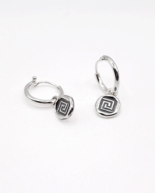 Silver hoop earrings with geometric Greek key charm on white background