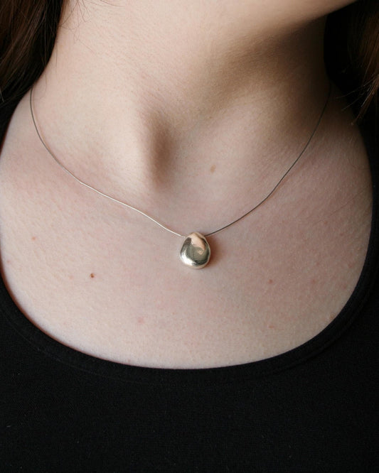 Necklace with a teardrop-shaped pendant worn by a person in a black top.