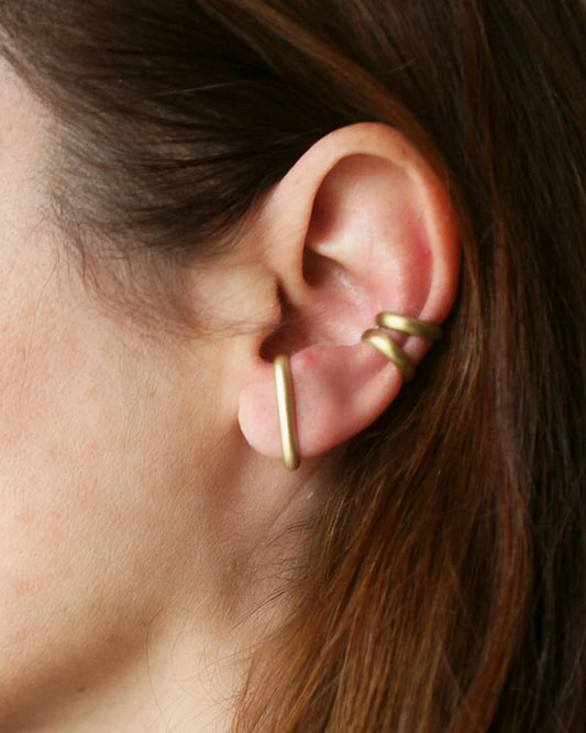 Gold ear cuff worn by a person with brown hair.