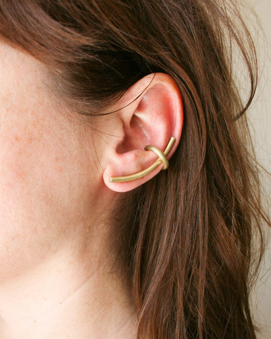Gold ear cuff worn by a person with brown hair.