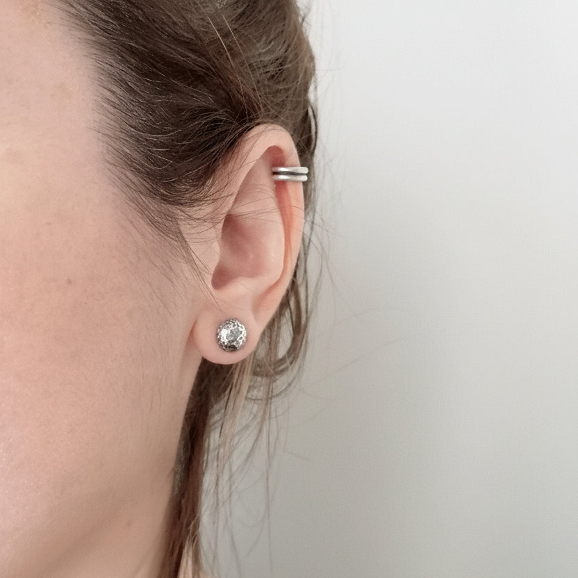 Close-up of a person wearing a silver earring with a clear gemstone on a plain background