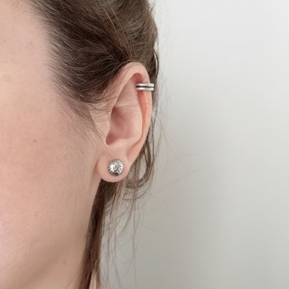 Close-up of a person wearing a silver earring with a clear gemstone on a plain background