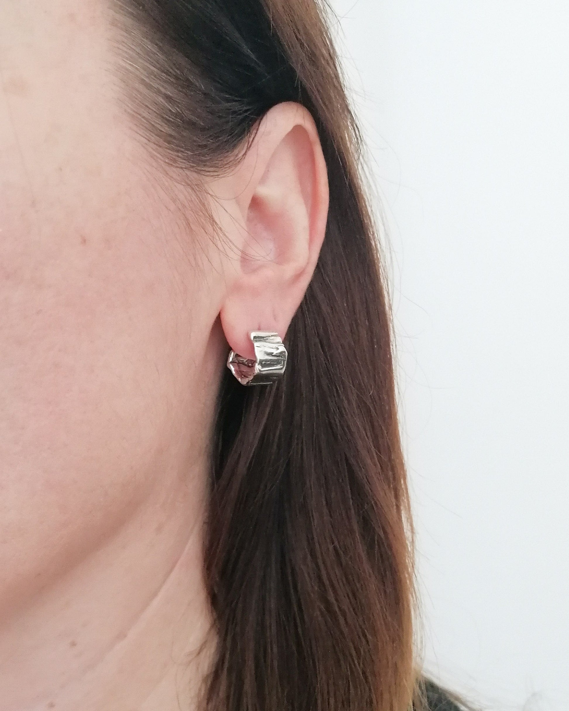Close-up of a person wearing a silver hoop earring against a neutral background
