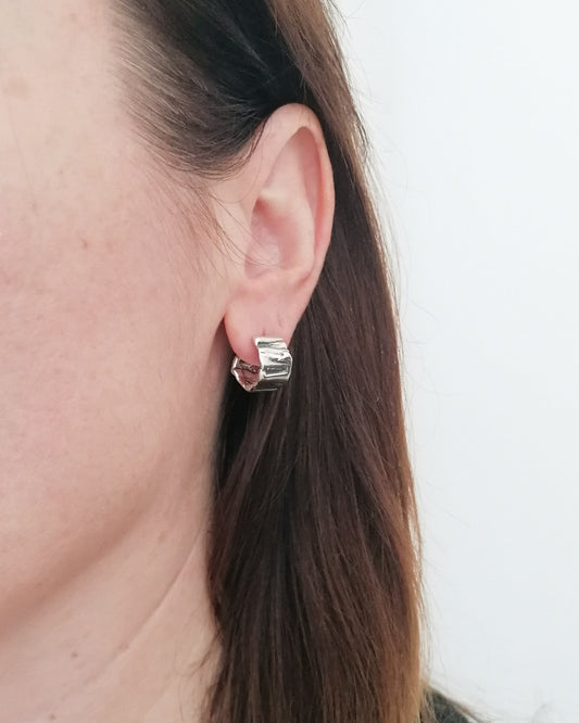 Close-up of a person wearing a silver hoop earring against a neutral background